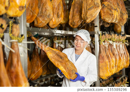 female worker checks the quality of jamon in a factory 135389296