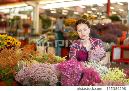 Middle-aged saleswoman holding bouquet of dry flowers in plants market Middle-aged saleswoman holding bouquet of dry flowers in plants market 135389298
