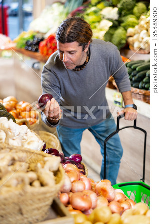 Adult man shopper chooses onions in shop 135389300