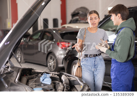 Woman car owner explains car engine problem to a car service mechanic 135389309