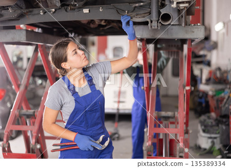 Female mechanic checking the rear suspension shock absorber of car 135389334