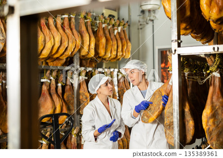 Two workers test the qualities of jamon in a factory Two workers test the qualities of jamon in a factory 135389361