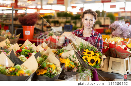 Middle-aged saleswoman holding bouquet of sunflowers Middle-aged saleswoman holding bouquet of sunflowers 135389362