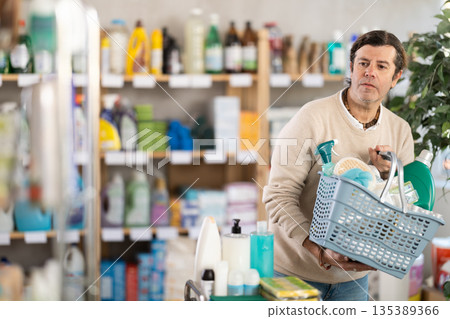 Man buyer with filled basket wanders around store, looking at display cases. 135389366