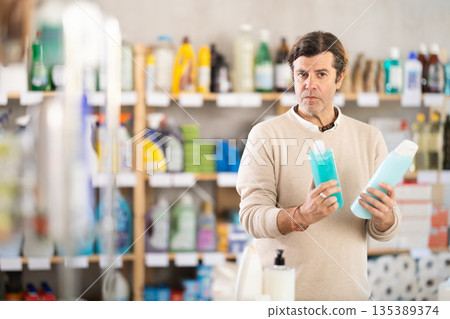 Man buyer chooses shampoo or shower gel in household goods department of supermarket 135389374