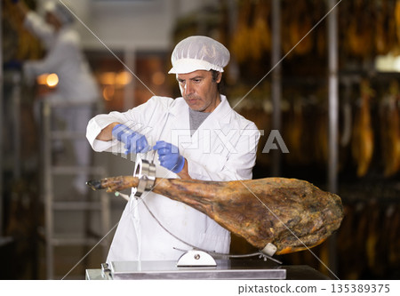 Male worker places jamon on jamonero to cut it into appetizing pieces 135389375