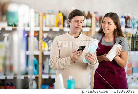 Saleswoman offering shower gel to man scanning barcode of bottles in store Saleswoman offering shower gel to man scanning barcode of bottles in store 135389385