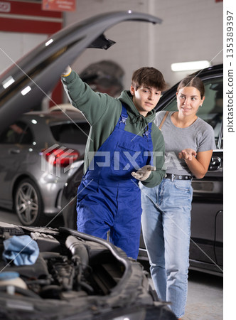 Auto technician explaining required car engine maintenance to female customer Auto technician explaining required car engine maintenance to female customer 135389397