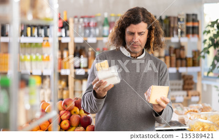 Choose cheese in supermarket - man chooses what cheese to buy in the dairy department section of store 135389421