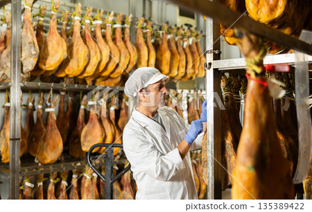 Male worker at ham factory checks the quality of ham in workshop 135389422