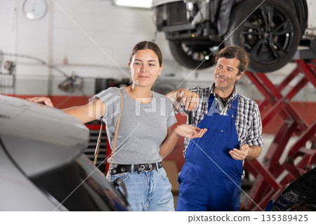 Auto mechanic giving car keys after repair to smiling girl 135389425