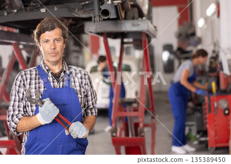 Auto mechanic standing with adjustable wrench in auto repair shop 135389450