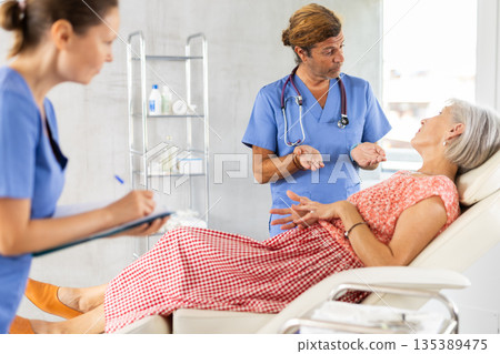 Doctor questioning senior woman, female assistant writing down answers 135389475