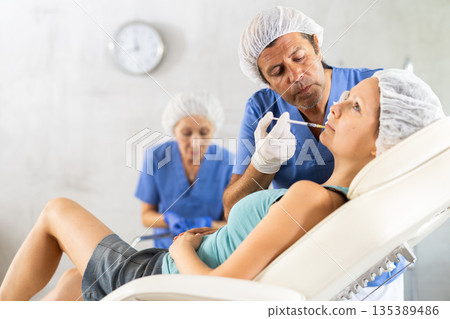 Male cosmetologist performing filler injections to correct lips contour to woman Male cosmetologist performing filler injections to correct lips contour to woman 135389486