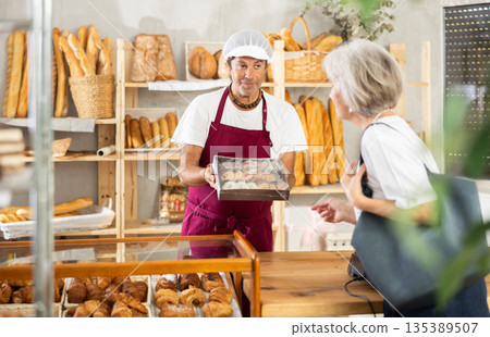 Male owner of bread shop shows for senior woman customer cookies in box Male owner of bread shop shows for senior woman customer cookies in box 135389507