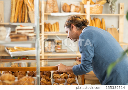 Male customer in casual clothes chooses croissants for breakfast in bakery 135389514
