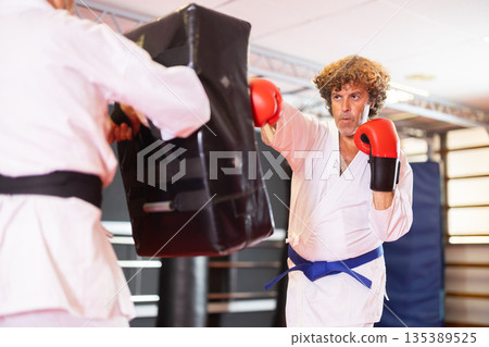 Karate student punching shield under guidance of experienced partner Karate student punching shield under guidance of experienced partner 135389525