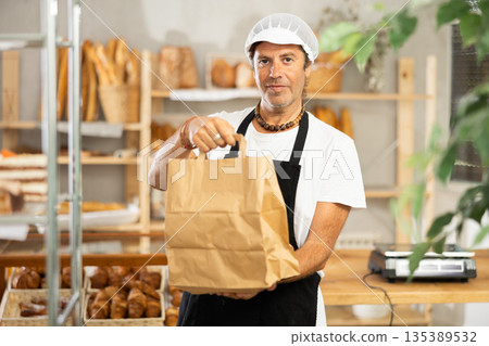 Middle-aged salesman holding paper bag in bakery 135389532