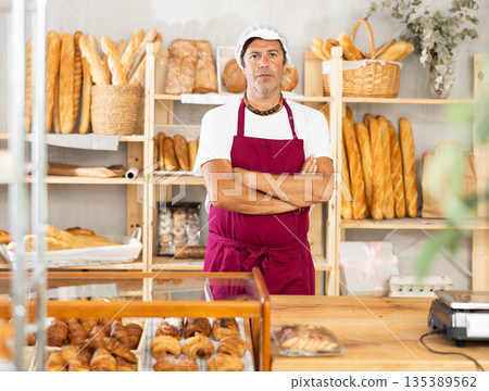 Portrait of friendly baker selling fresh baguettes and croissants in bakery Portrait of friendly baker selling fresh baguettes and croissants in bakery 135389562