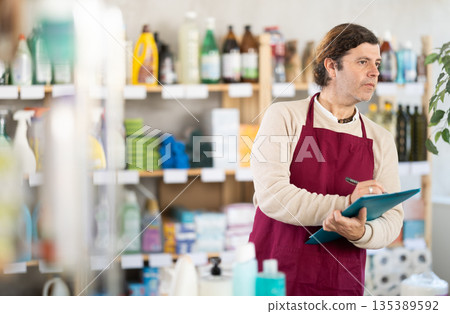 Man seller, with paper and invoice in hands, make inventory in store. 135389592