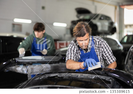 Experienced auto body technician sanding car parts in workshop 135389615