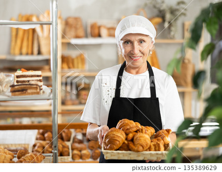 Elderly woman baker offers to buy a fresh croissants 135389629