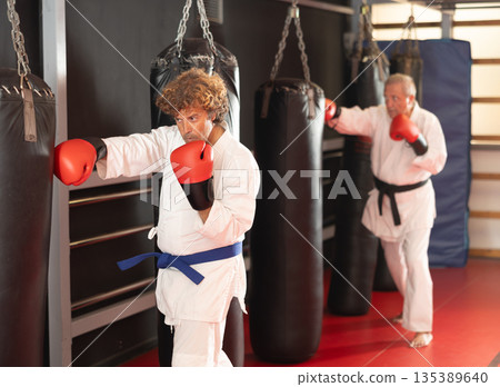 Man punching heavy bag in martial arts class Man punching heavy bag in martial arts class 135389640