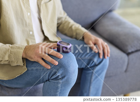 Man using pulse oximeter on finger to monitor oxygen saturation in blood at home 135389778