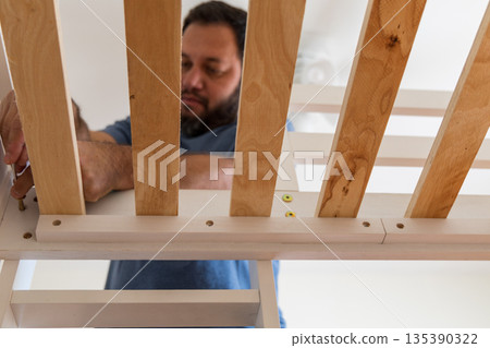 A man is working on a bed frame, tightening screws and adjusting the slats 135390322