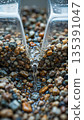 Clear water flowing over colorful pebbles. Clear water flows in a narrow stream over a bed of colorful, smooth pebbles, including shades of gray, orange, and beige. 135391047