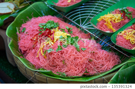 Traditional Thai Pink Noodles or Mee Kati served on banana leaves. Vibrant pink rice vermicelli topped with shredded egg and chili, a popular authentic Thai street food 135391324