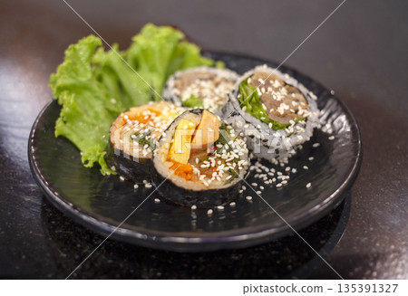 Traditional Korean Gimbap and Sushi rolls with fresh vegetables, egg, and sesame seeds served on a black plate. Healthy Asian cuisine food photography for background Traditional Korean Gimbap and Sushi rolls with fresh vegetables, egg, and sesame seeds served on a black plate. Healthy Asian cuisine food photography for background 135391327