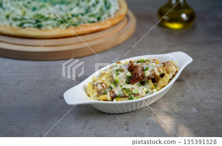 Gourmet loaded French fries with melted cheese, crispy bacon, and green onions in a white bowl. Comfort food concept for restaurant menus, snacks, and fast food appetizers Gourmet loaded French fries with melted cheese, crispy bacon, and green onions in a white bowl. Comfort food concept for restaurant menus, snacks, and fast food appetizers 135391328