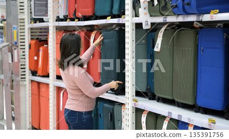 Young female shopper comparing different suitcases in a travel goods section, making luggage choice and vacation planning Young female shopper comparing different suitcases in a travel goods section, making luggage choice and vacation planning 135391756
