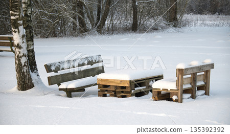 Wooden benches and pallet table covered in fresh snow in a serene winter park setting 135392392
