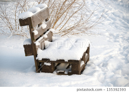 Wooden pallet bench covered in fresh snow on a bright winter day Wooden pallet bench covered in fresh snow on a bright winter day 135392393