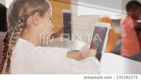 Schoolgirl sitting at school desk viewing code overlay on tablet computer, with blurred classmate Schoolgirl sitting at school desk viewing code overlay on tablet computer, with blurred classmate 135392573