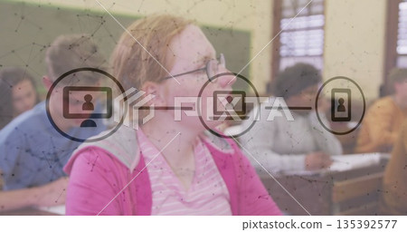 Listening hoodie-wearing student with glasses attending lesson in classroom with network overlay Listening hoodie-wearing student with glasses attending lesson in classroom with network overlay 135392577