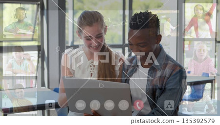 Smiling teenager and tutor studying silver laptop at desk, with online calls and chalkboard overlay 135392579