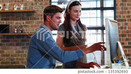 Reviewing financial charts coworkers in business attire using computer in brick walled workspace 135392693