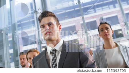 Standing business professionals displaying digital charts in glass-walled atrium with steel columns Standing business professionals displaying digital charts in glass-walled atrium with steel columns 135392703