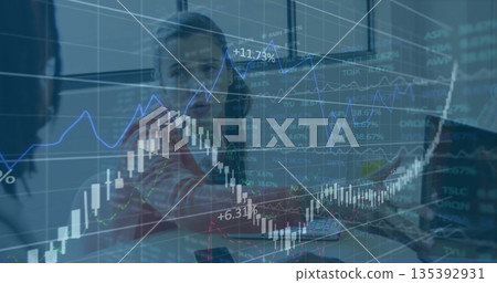 Professionals pointing at stock trends in office, candlestick graphs on translucent screen 135392931