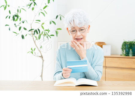 Senior woman thinking while looking at her bankbook Senior woman thinking while looking at her bankbook 135392998