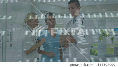 Three doctors in scrubs and lab coats reviewing data on tablet in clinic room with stethoscopes 135392999