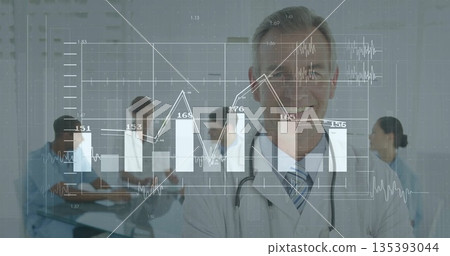 Standing male doctor wearing stethoscope presenting data at hospital conference table showing chart 135393044