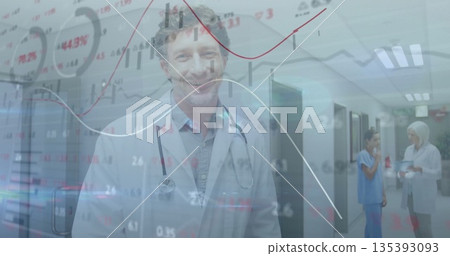 Smiling mature male physician examining floating data graphs in hospital corridor, with stethoscope 135393093