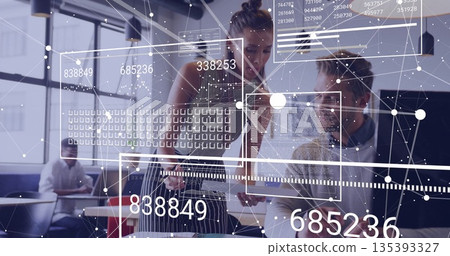 Coworkers examining tablet and analyzing data overlays in open plan office, with laptop documents 135393327