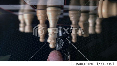 Grasping dark pawn between finger and thumb on glossy chessboard, with light pawn row behind Grasping dark pawn between finger and thumb on glossy chessboard, with light pawn row behind 135393491