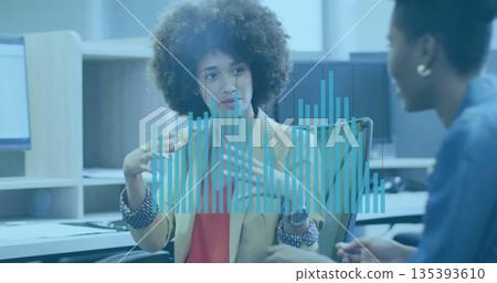 Gesturing curly haired woman wearing blazer explaining data overlay in office, with monitors Gesturing curly haired woman wearing blazer explaining data overlay in office, with monitors 135393610
