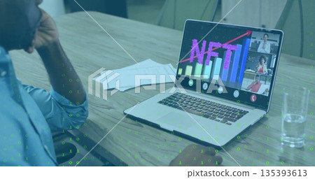 Watching blue-shirted man analyzing NFT chart on laptop at conference table, with papers  and  water 135393613